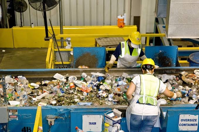 Workers sorting plastic waste on conveyor belt at recycling facility
