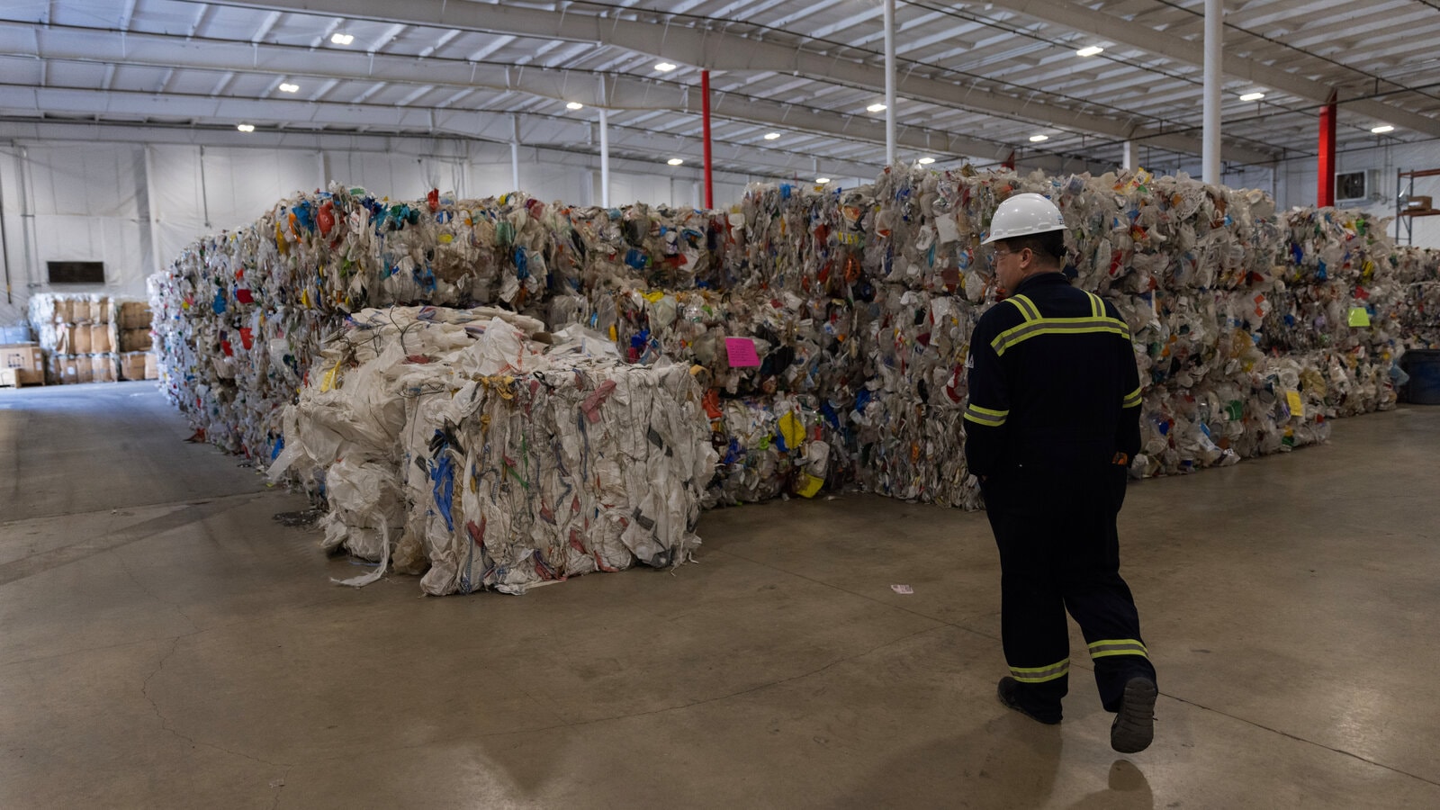 Recycling facility warehouse with baled plastic waste and worker in safety gear